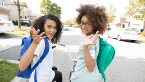 two girls with backpacks waving