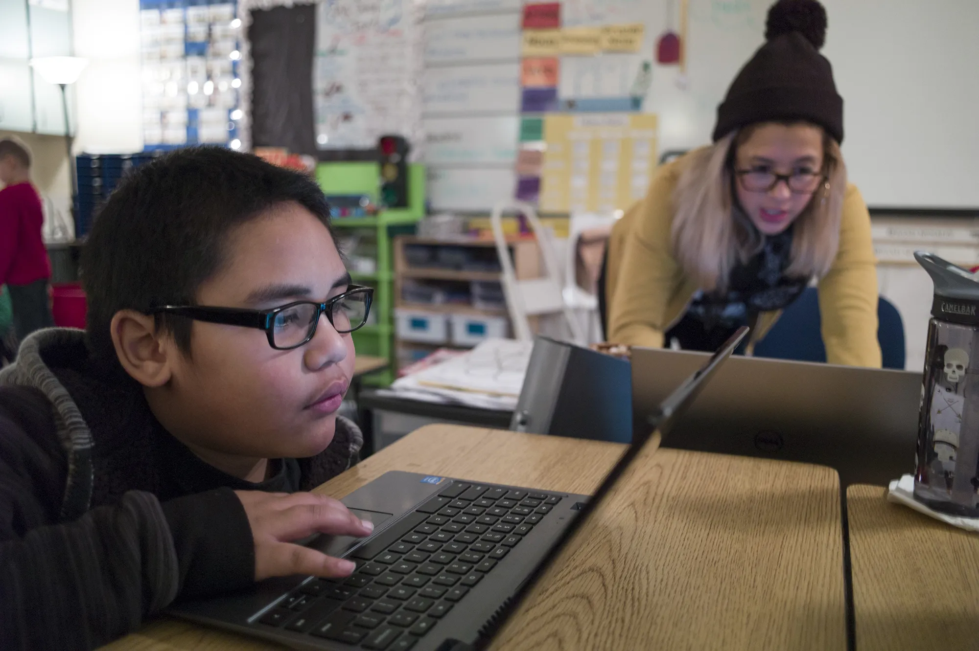 student works on laptop with teacher instructing nearby