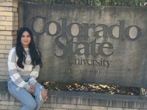 girl sits in front of college sign