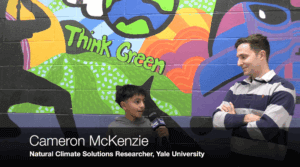A young boy interviews a man in front of a colorful mural reading Think Green. Text on image: Cameron McKenzie, Natural Climate Solutions Researcher, Yale University.
