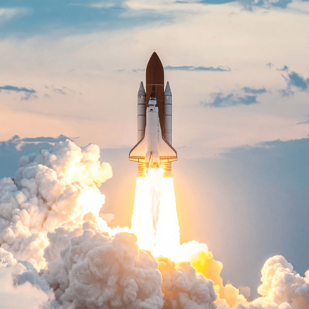 A space shuttle launches into the sky, producing bright flames and thick clouds of smoke against a backdrop of clouds and blue sky.