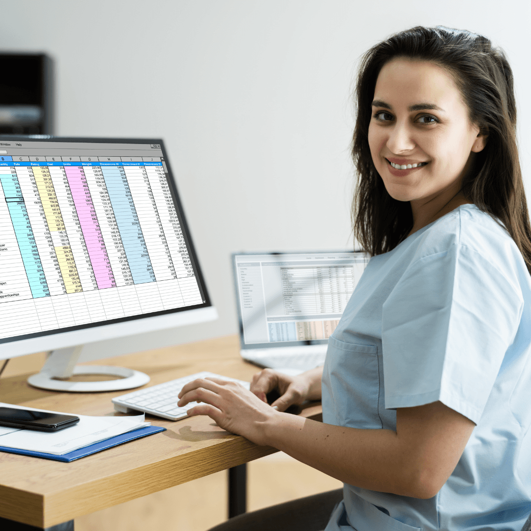 A woman in scrubs smiles at her desk while working on a computer displaying a colorful spreadsheet from the Launching Futures Toolkit. A laptop and notepad are also on the desk.