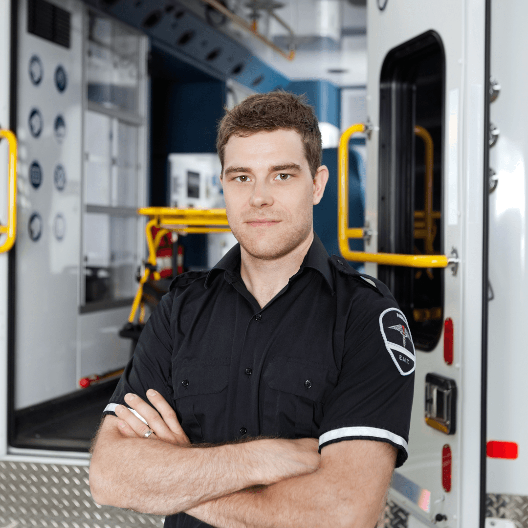 A paramedic in uniform stands with arms crossed in front of an open ambulance, looking confidently at the camera, embodying the spirit of the Launching Futures Toolkit.