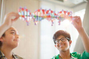 Two students smiling and holding up a colorful DNA model together in a bright classroom setting, exploring discovery with the Launching Futures Toolkit.