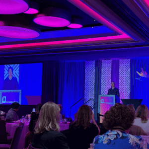A man speaks from a podium at the Grantmakers for Education conference, with his image projected on a large screen behind him.